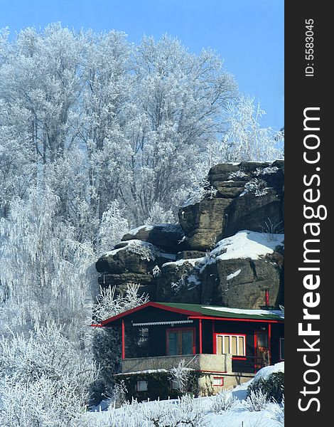 Romantic  snowy scenery cottage below rock