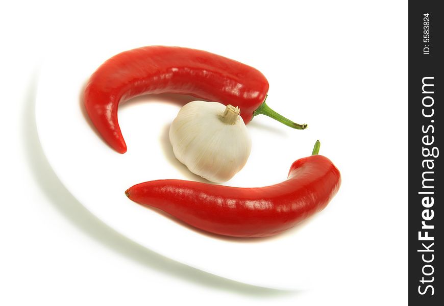 Two fresh chili peppers and a bulb of garlic on a white plate and isolated on white background. Two fresh chili peppers and a bulb of garlic on a white plate and isolated on white background