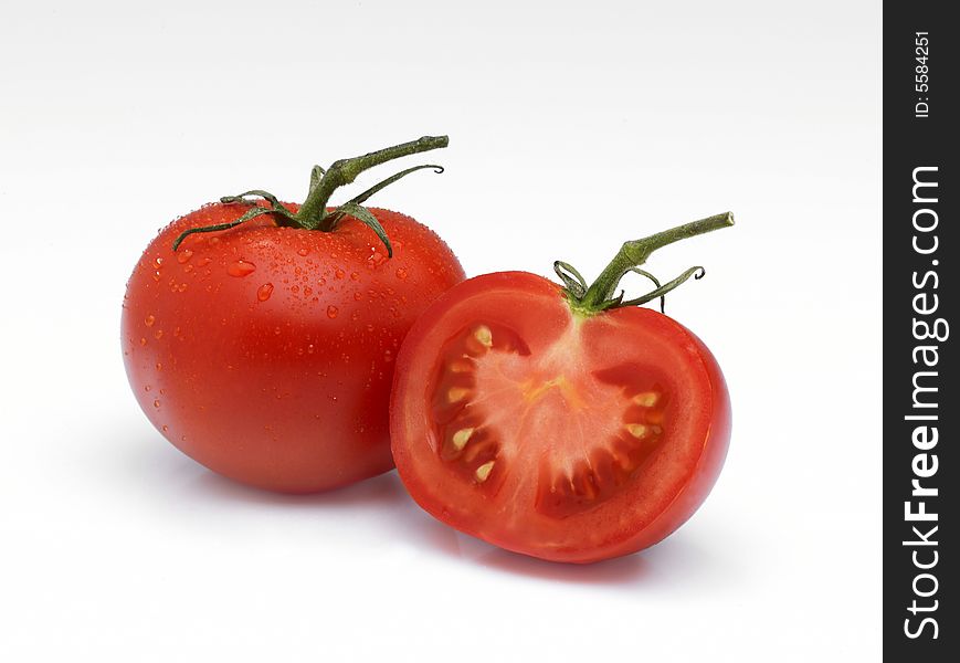 An arrangement of a whole Tomato and a half on a white background with water droplets and stalks. An arrangement of a whole Tomato and a half on a white background with water droplets and stalks.