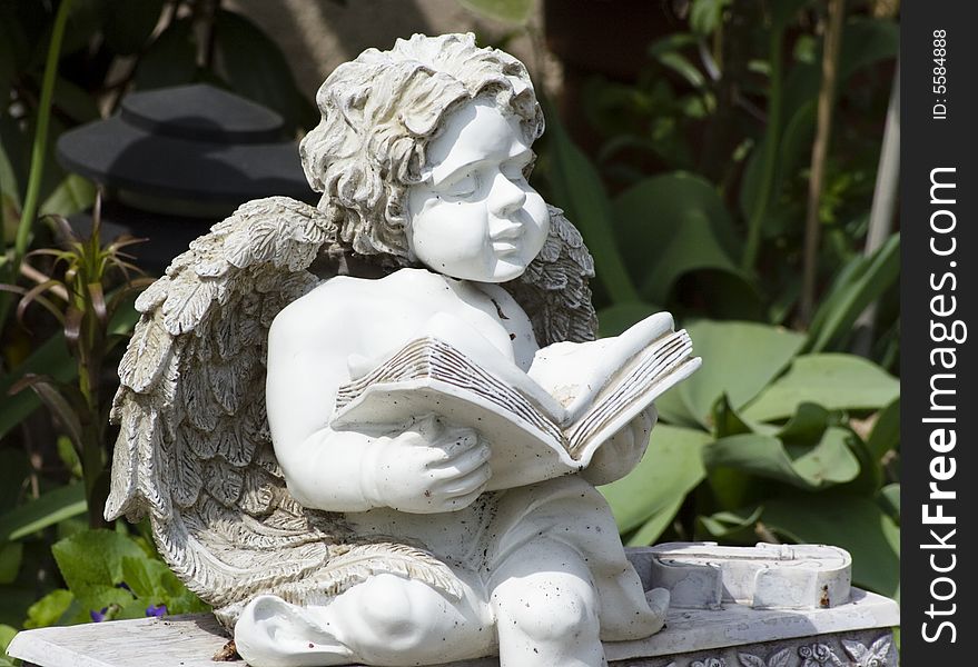 Statue of sitting and reading angel at the flowering garden