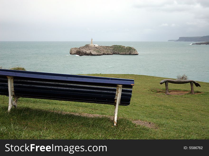 Bench looking to a island with a lighthouse on the entrance to a bay of Santander