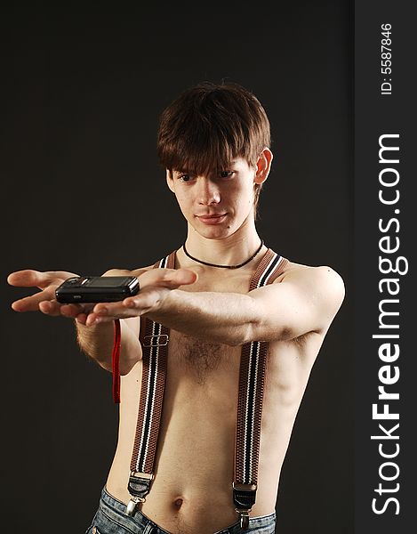 Cute man  with nude torso wearing jeans with braces shows some electronic or cell phone. Cute man  with nude torso wearing jeans with braces shows some electronic or cell phone