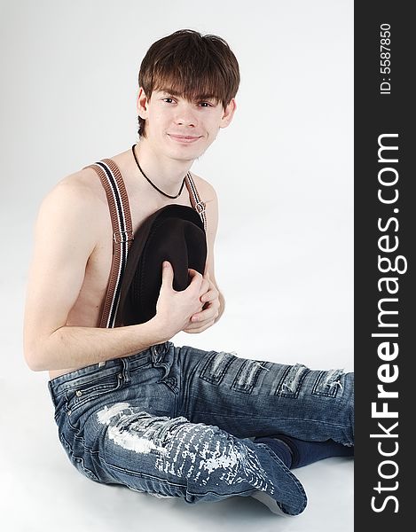 Cute man wearing jeans with naked torso sits and holds a hat. Cute man wearing jeans with naked torso sits and holds a hat