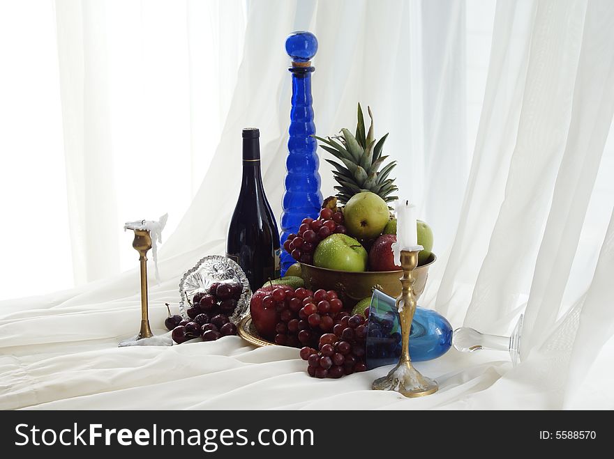 Red wine candlesticks blue goblets and brass overflowing fruit bowl. Red wine candlesticks blue goblets and brass overflowing fruit bowl.