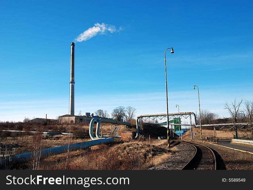 Industrial plant with pipes leading to chimney and railroad