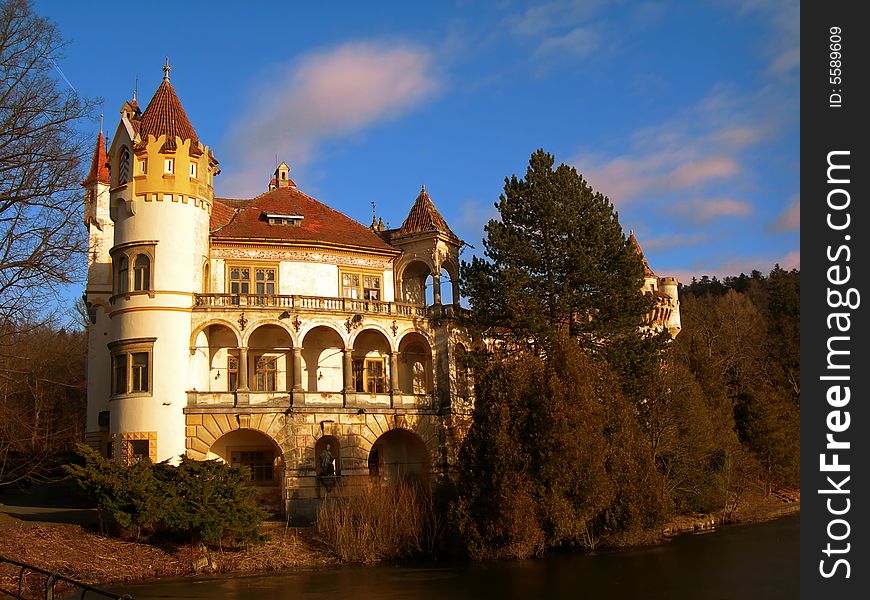 Beautiful romantic castle with river and forest at sunset