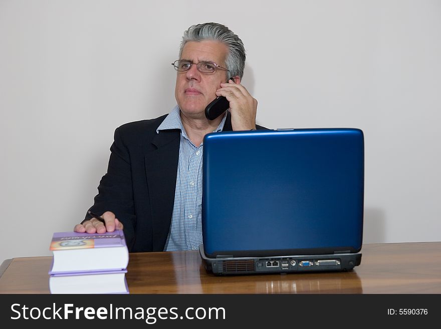 A businessman working in his study with a computer and a mobile. A businessman working in his study with a computer and a mobile