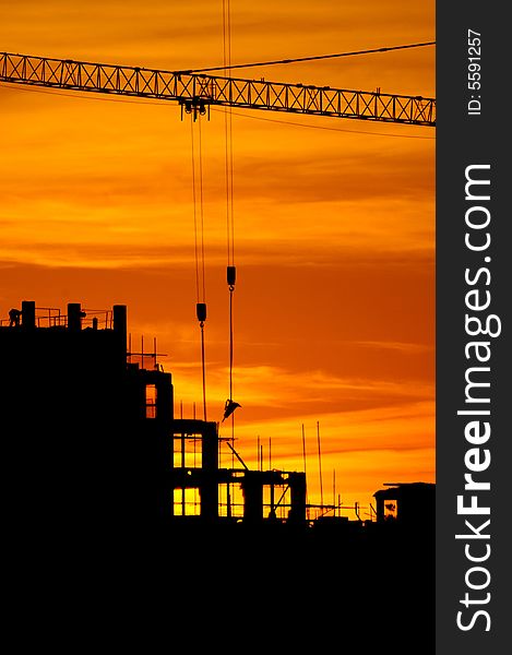 Construction of a building, cranes and other machinery as silhouettes against a background of red sunset sky. Construction of a building, cranes and other machinery as silhouettes against a background of red sunset sky