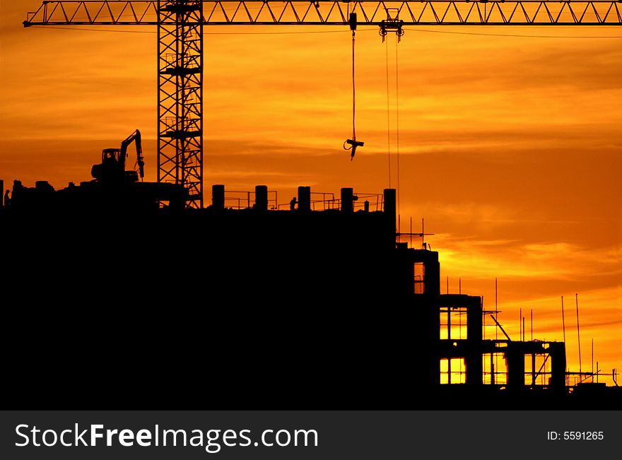 Construction of a building, cranes and other machinery as silhouettes against a background of red sunset sky. Construction of a building, cranes and other machinery as silhouettes against a background of red sunset sky