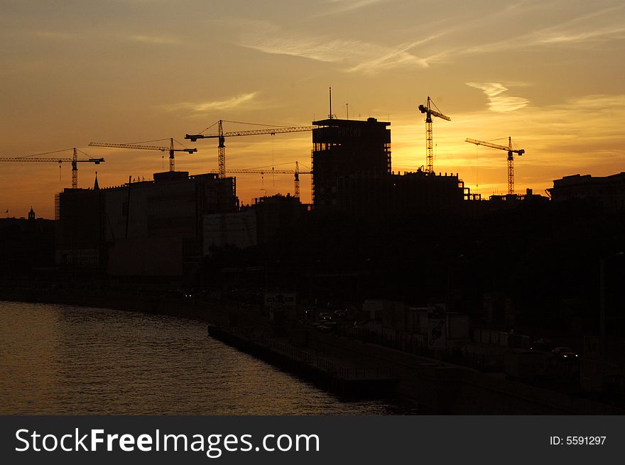 Construction of a building, cranes and other machinery as silhouettes against a background of red sunset sky. Construction of a building, cranes and other machinery as silhouettes against a background of red sunset sky