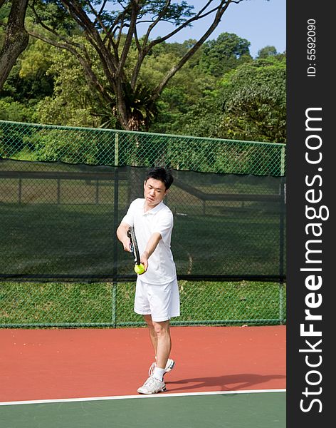 An Asian male tennis player is teeing off at the tennis court, wearing white tennis clothes. An Asian male tennis player is teeing off at the tennis court, wearing white tennis clothes.