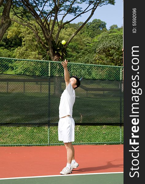 An Asian male tennis player is teeing off at the tennis court, wearing white tennis clothes. An Asian male tennis player is teeing off at the tennis court, wearing white tennis clothes.