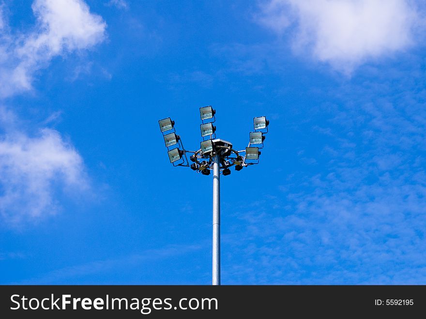 A single floodlight with blue sky and white clouds as the backgound at the corner of the football field.