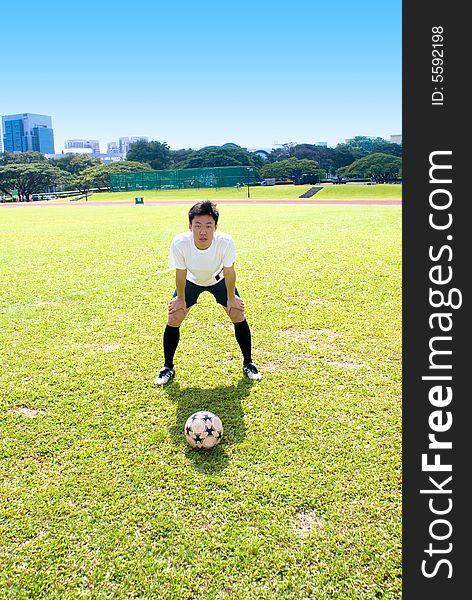 Asian Football player with football in the green court with blue sky