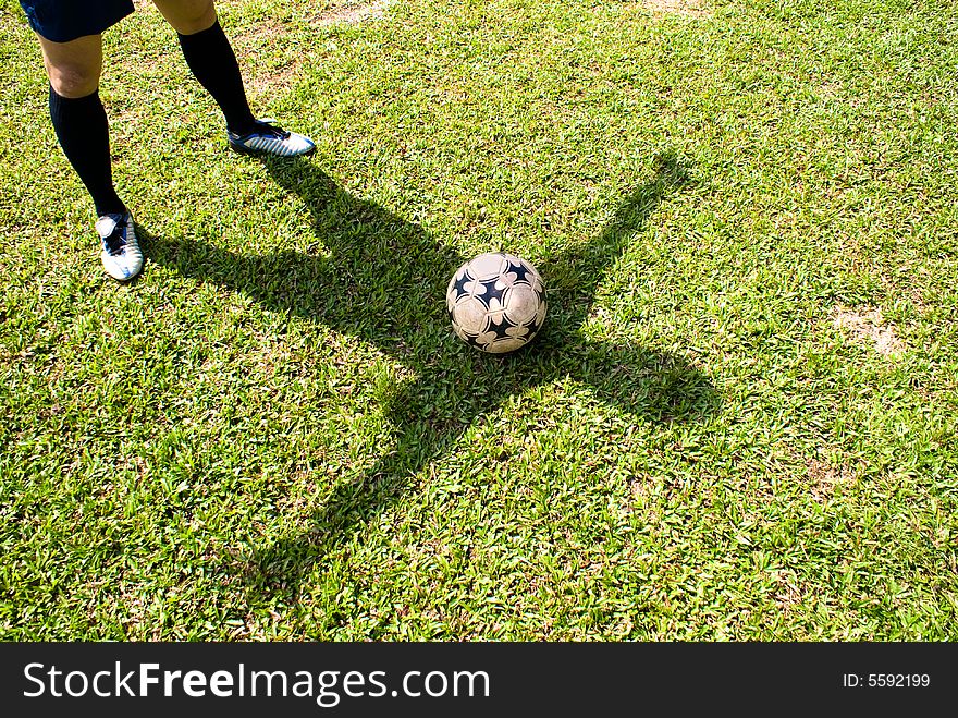 The shadow of a asian football player together with a football on green grass. The shadow of a asian football player together with a football on green grass