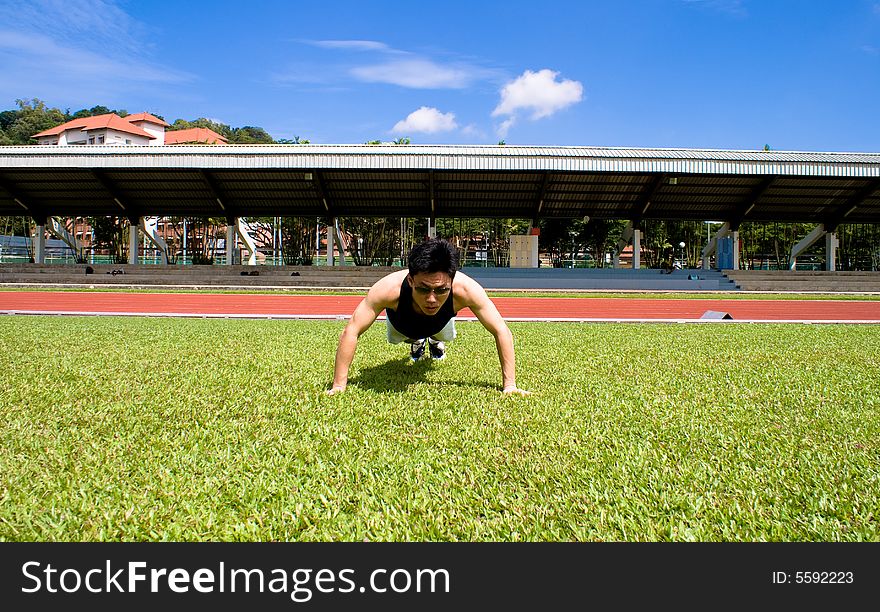 An asian male athlete is doing some preparation in the green grass field.