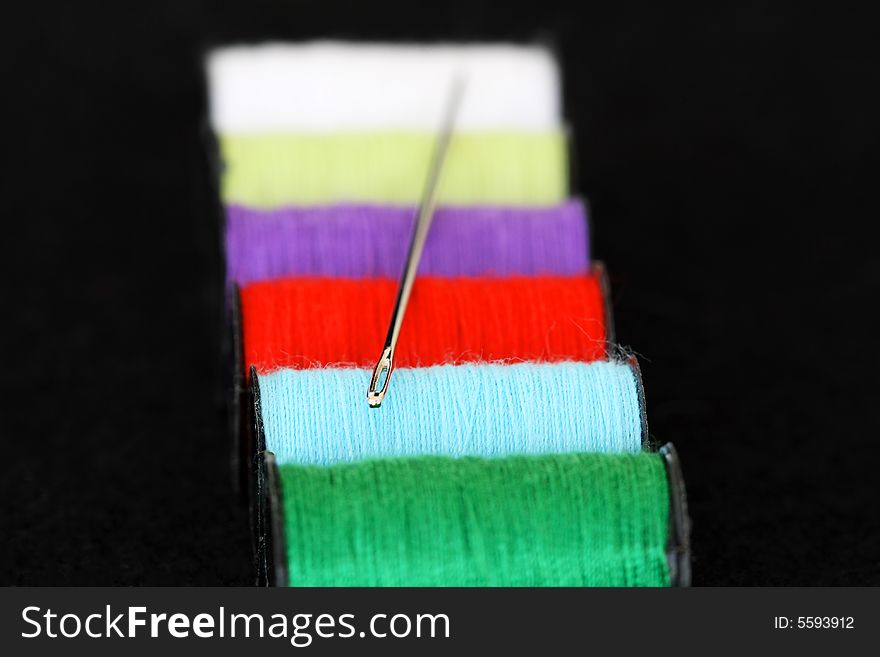 Spools of cotton and a needle on a black background. Spools of cotton and a needle on a black background.