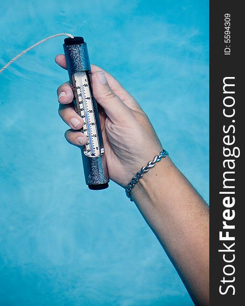 Female hand holding pool thermometer under water