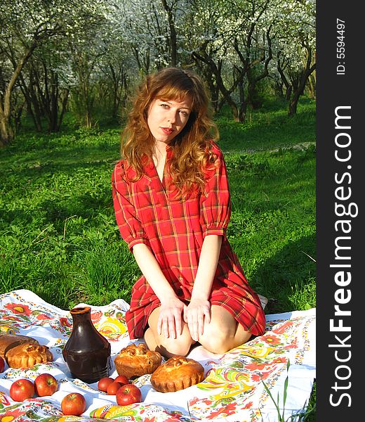 The young red-haired woman is having a picnic in the spring garden. The young red-haired woman is having a picnic in the spring garden