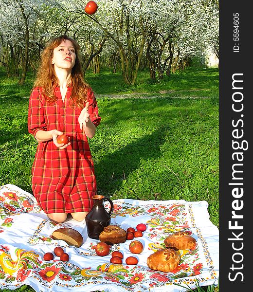 The young red-haired woman is juggling apples in the spring garden. The young red-haired woman is juggling apples in the spring garden