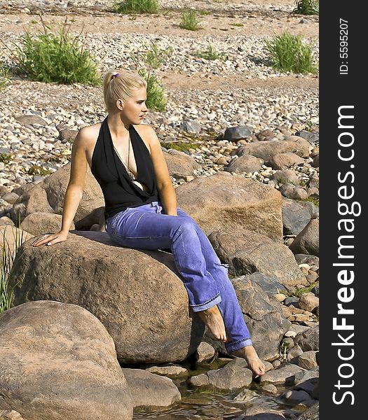 Beautiful blond girl sitting on a stone near the sea. Beautiful blond girl sitting on a stone near the sea