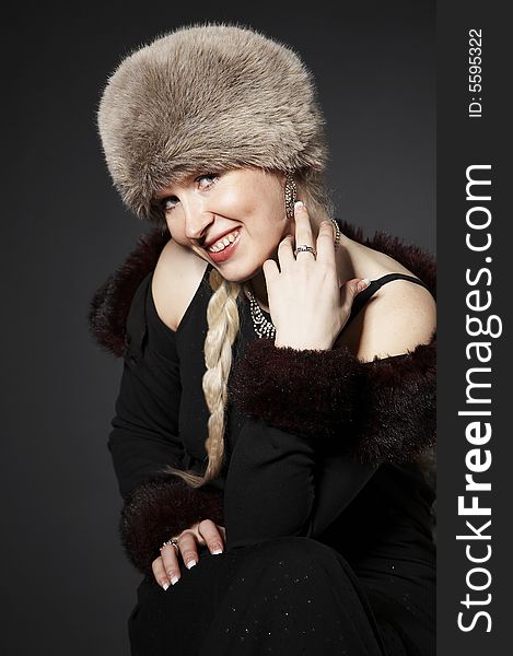 Portrait of a smiling young girl wearing fur winter hat and jewelery on a dark background. Portrait of a smiling young girl wearing fur winter hat and jewelery on a dark background