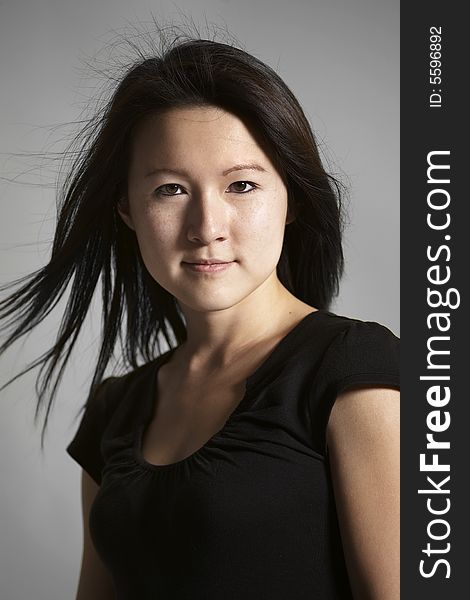 Head and shoulders portrait of young Asian woman against a gray background.