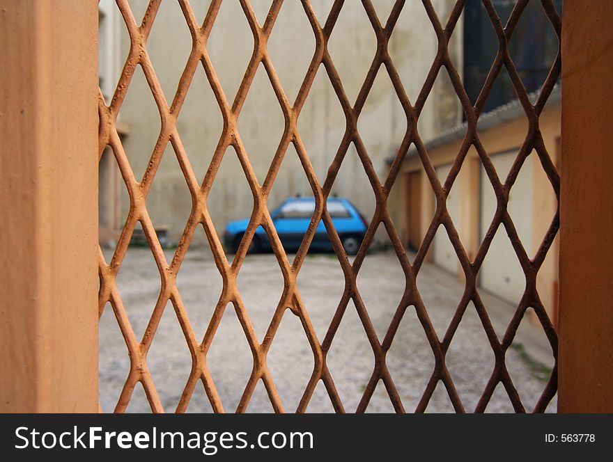 An out of focus renault 5 seen through a metal meshed gate