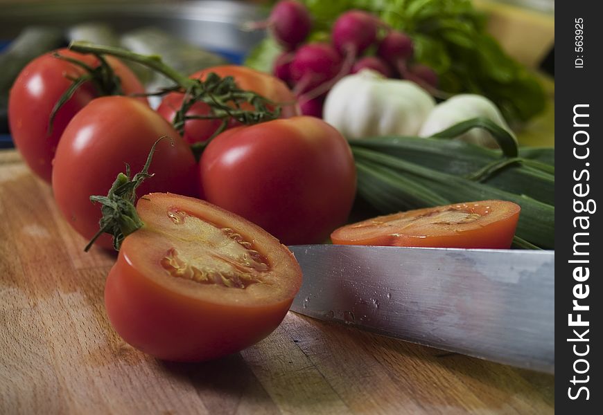 Cutting Tomatoes at kitchean board, vegetables at background