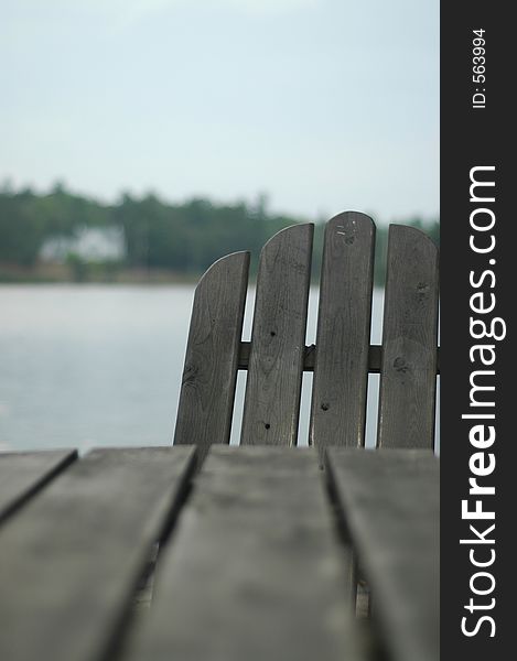 Adirondack chair hiding behind table . Focus is on the chair, with cottage in background. Adirondack chair hiding behind table . Focus is on the chair, with cottage in background