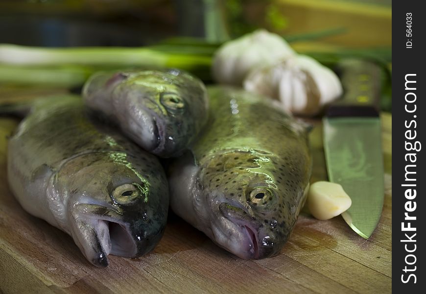 Three fresh trouts at kitchen cutting board, vegetables at background. Three fresh trouts at kitchen cutting board, vegetables at background