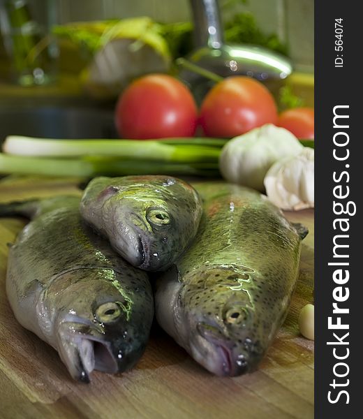 Three fresh trouts at kitchen cutting board, vegetables at background. Three fresh trouts at kitchen cutting board, vegetables at background