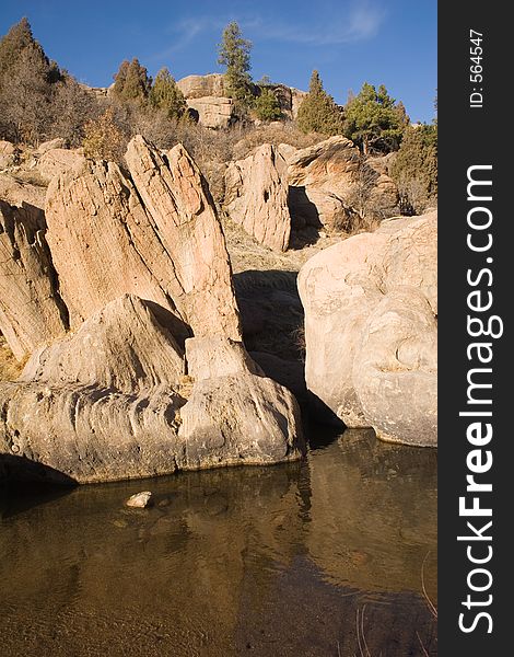 Unusual rock formations loom over a clear, calm pool of water in Castlewood Canyon of central Colorado. Unusual rock formations loom over a clear, calm pool of water in Castlewood Canyon of central Colorado.