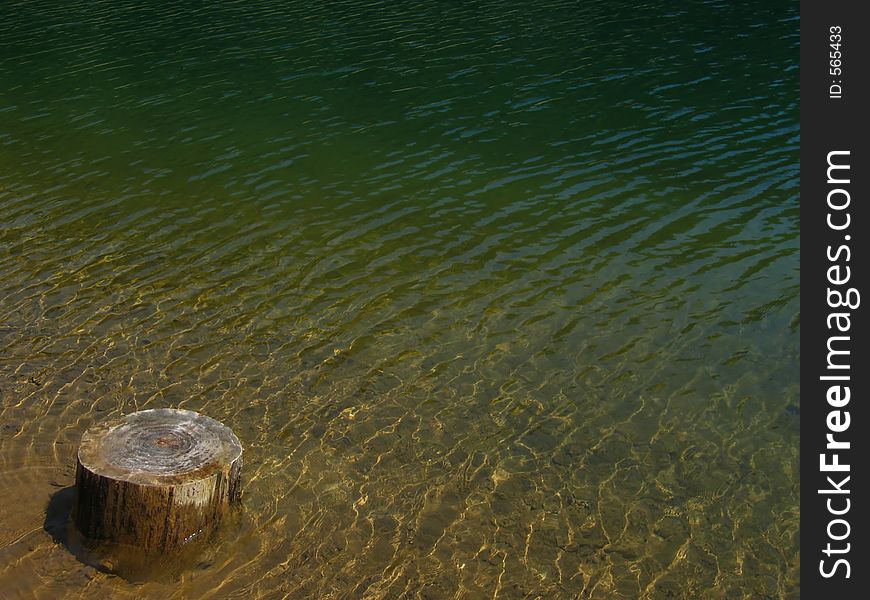 Shallow water of the mountain lake with a tree-stump in the foreground