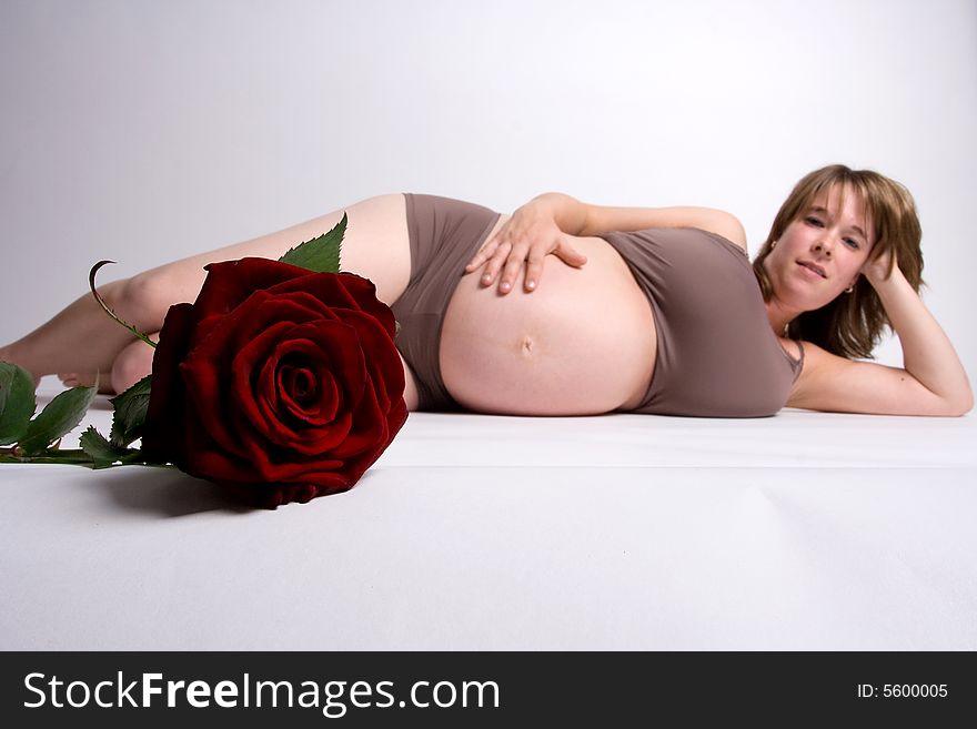 A pregnant woman lying on the floor and holding her belly with red rose in the front.