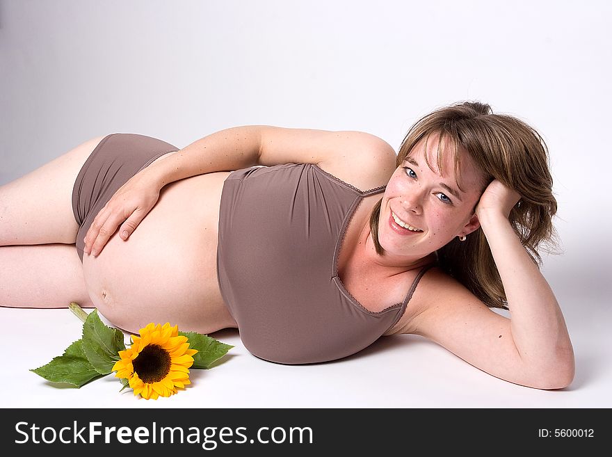 A pregnant woman lying on her side and holding her head. Next to her lies a sun flower.