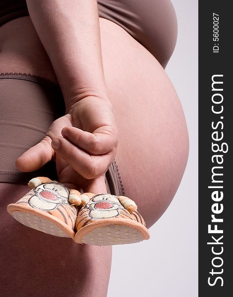 Little shoes holded in the fingers of a pregnant mother. Little shoes holded in the fingers of a pregnant mother