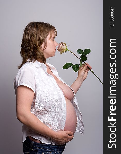 A pregnant woman holding her belly and smelling a pink rose. A pregnant woman holding her belly and smelling a pink rose