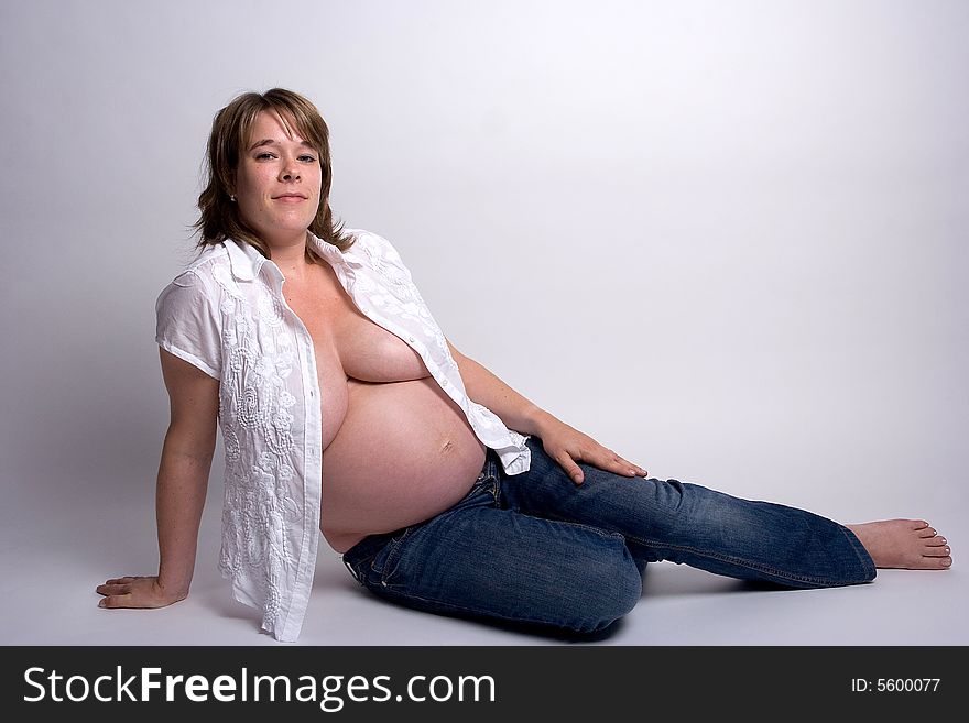 A pregnant woman on her side with jeans and a white shirt on!. A pregnant woman on her side with jeans and a white shirt on!