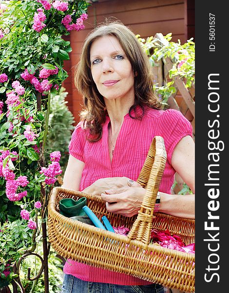 Woman in front of a rose tree holding bag with garden utensils. Woman in front of a rose tree holding bag with garden utensils