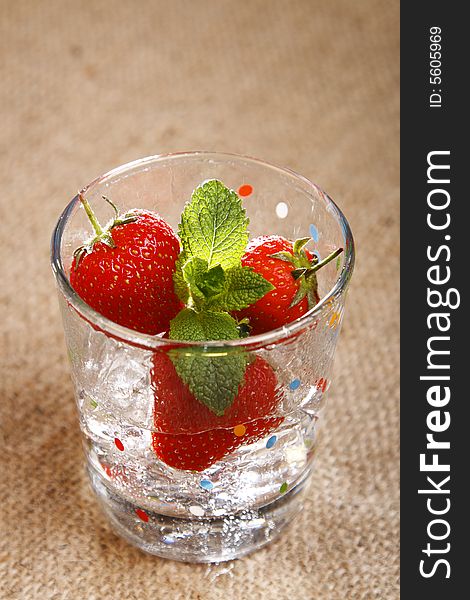 Strawberry, mint, ice cubes and water in wet glass on burlap canvas background
