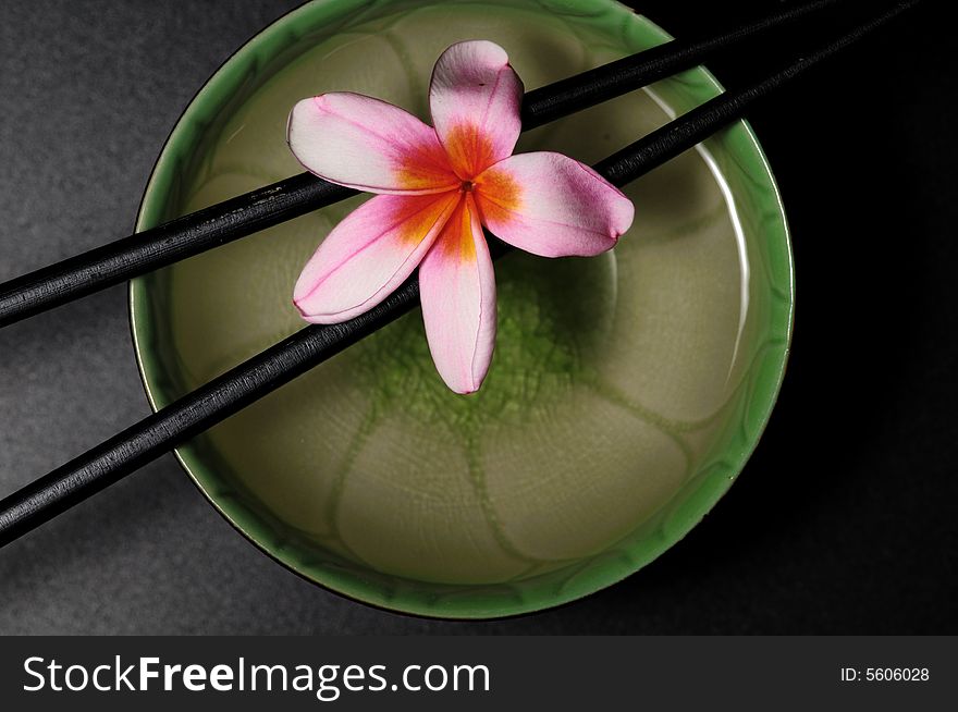 A zen composition with chopstick hold a flower over the water