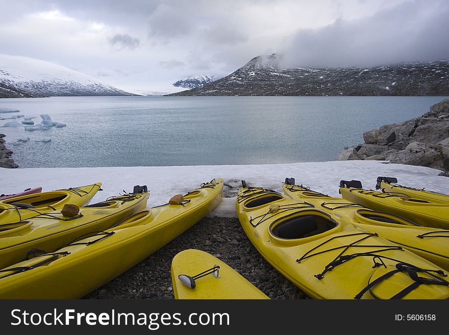 Several yellow kayaks on the beach with snow capped mountains on Jostedalsbreen glacier. Several yellow kayaks on the beach with snow capped mountains on Jostedalsbreen glacier