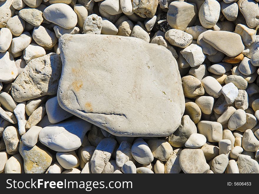 Larger, flat, gray stone on top of smaller light grey pebbles. Larger, flat, gray stone on top of smaller light grey pebbles