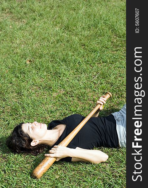 A woman is laying on the grass in the park.   Her eyes are closed and she appears to be sleeping.  She is holding a baseball bat across her chest.  Vertically framed photo. A woman is laying on the grass in the park.   Her eyes are closed and she appears to be sleeping.  She is holding a baseball bat across her chest.  Vertically framed photo.