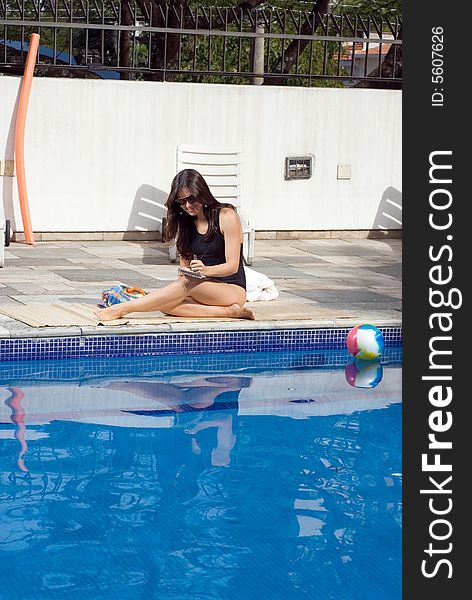 A female, writing in a notebook, smiling, sitting on the poolside floor - vertically framed. A female, writing in a notebook, smiling, sitting on the poolside floor - vertically framed