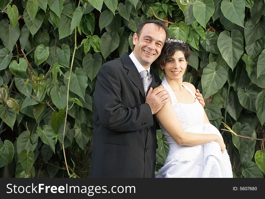 Newly weds smile at the camera while holding each other, in their wedding clothes. - vertically framed. Newly weds smile at the camera while holding each other, in their wedding clothes. - vertically framed