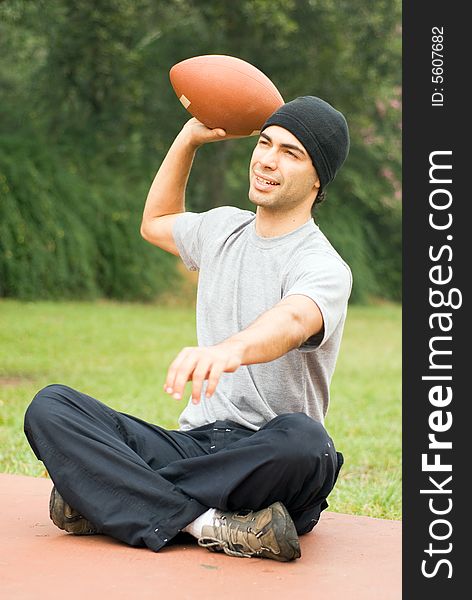 A man sitting, preparing to throwing a football, at a park, smiling. - vertically framed. A man sitting, preparing to throwing a football, at a park, smiling. - vertically framed