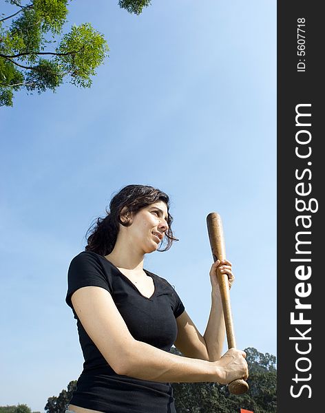 A woman is at a park holding a baseball bat.  Vertically framed photo. A woman is at a park holding a baseball bat.  Vertically framed photo.