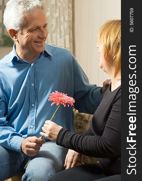 A couple staring at each other, holding a pink flower, smiling. - vertically framed. A couple staring at each other, holding a pink flower, smiling. - vertically framed